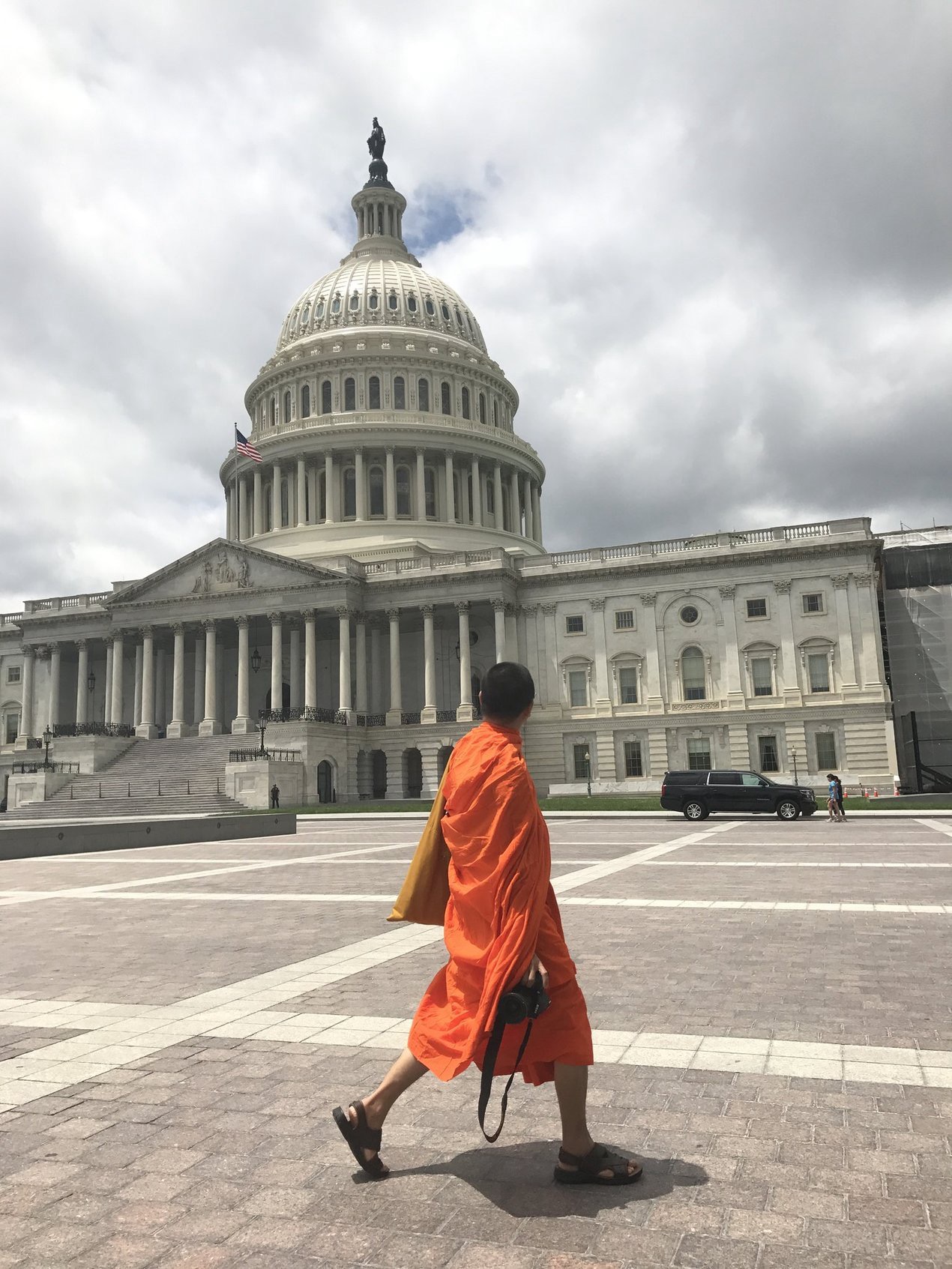 A Buddhist monk carrying a camera walks in front of the United States Capitol